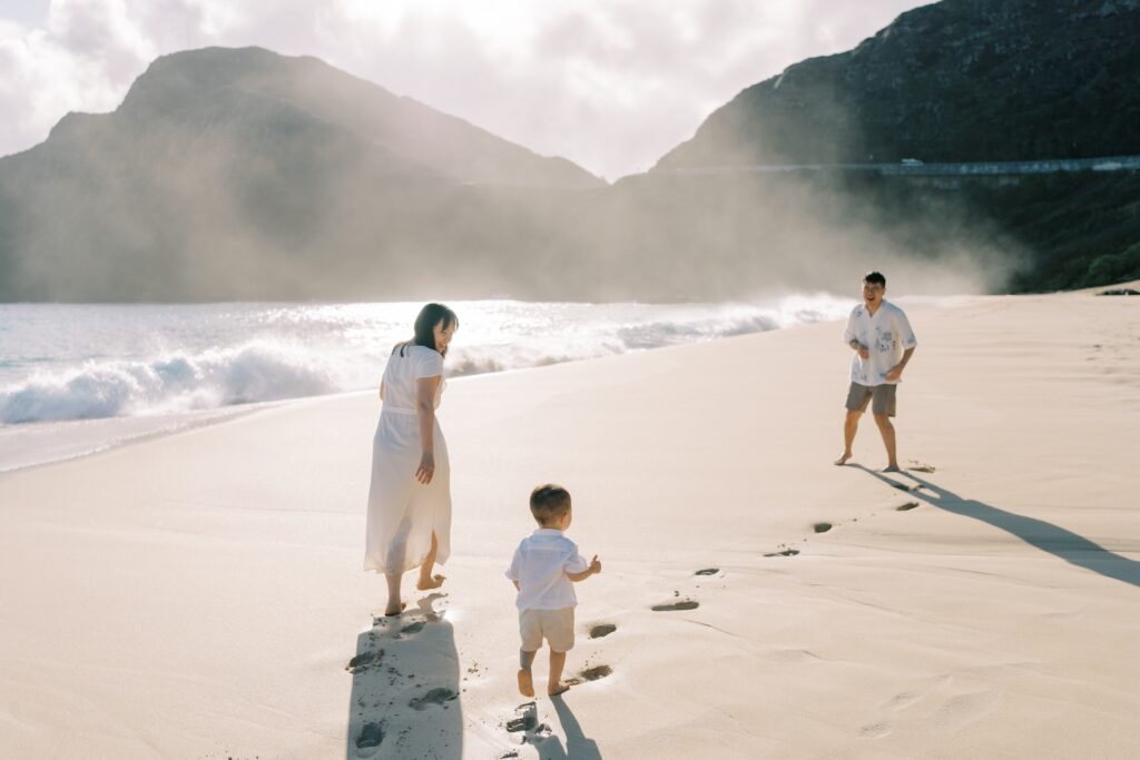 Little boy running across the sand toward his parents during a sunrise family beach session on Oahu.