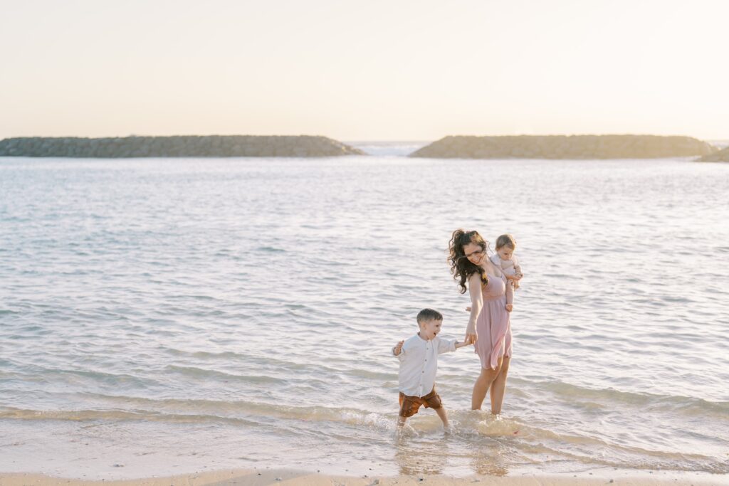 Mom walking in the shallow ocean with her young children during a relaxed family beach photoshoot.