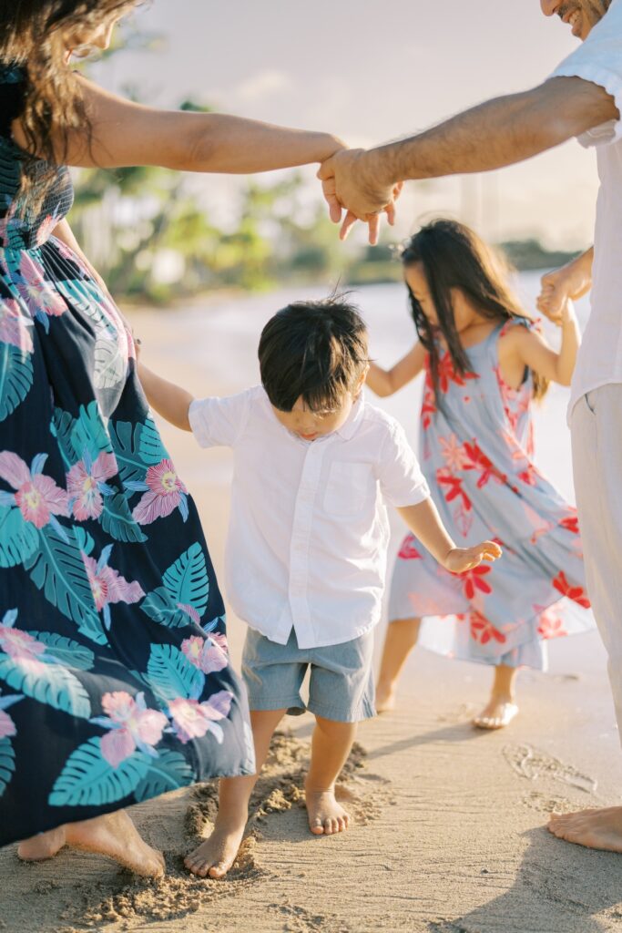 Family of four standing barefoot at the shoreline during a beach photo session on Oahu.