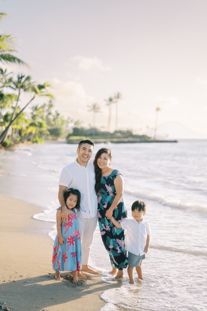 Family of four standing barefoot at the shoreline during a beach photo session on Oahu.