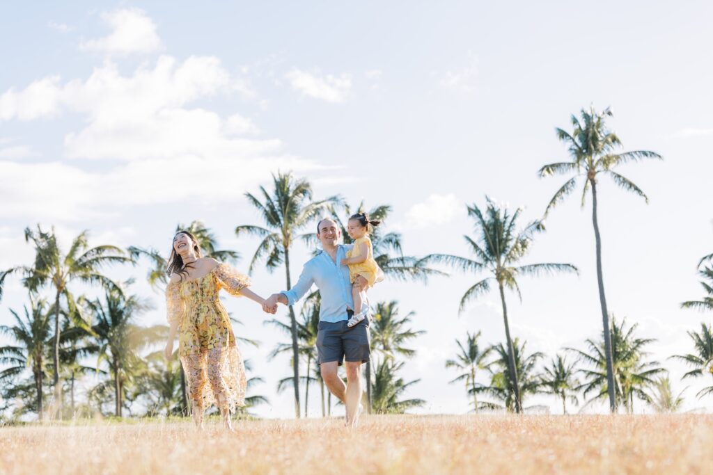 Parents walking hand in hand while carrying their toddler during a relaxed family photo session in Hawaii